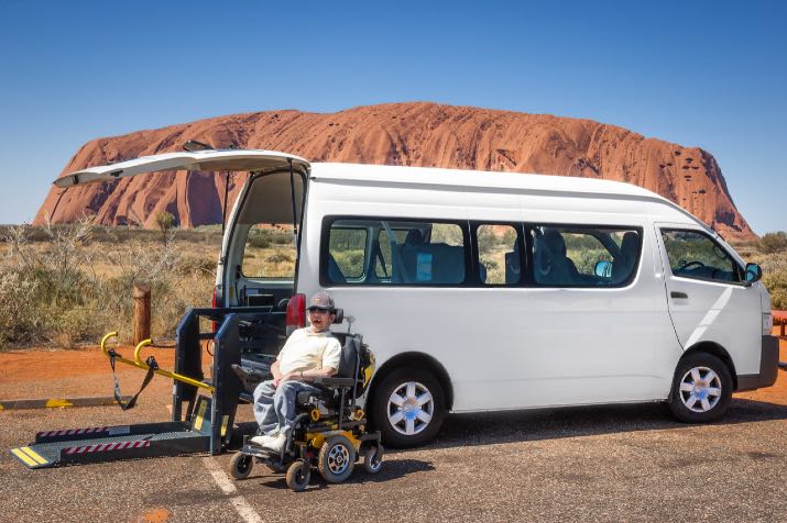 Van parked in front of Uluru with a man in a wheelchair sitting in front