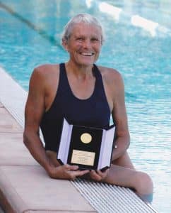 Lyn Lillecrapp holding her Order of Australia medal sitting on the edge of a pool