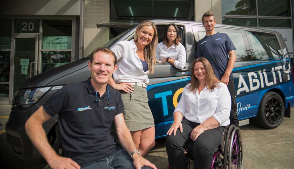 Five people sitting and standing in front of the Total Ability van smiling