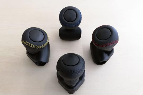 Four leather standard spinner knobs with various coloured stitching bunched together on a surface.