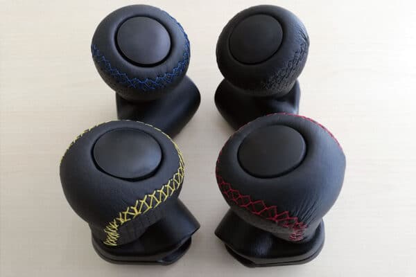 Four leather standard spinner knobs with various coloured stitching bunched together on a surface.