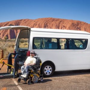 Van parked in front of Uluru with a man in a wheelchair sitting in front